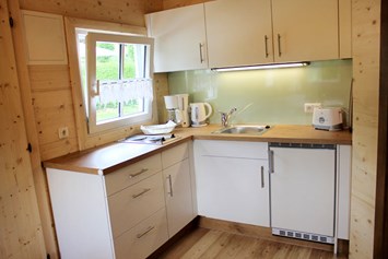 Glamping: Ferienhütte "Drachenwand": kleine Küche mit Kühlschrank, Kochgelegenheit, Kaffeemaschine, Wasserkocher, Toaster, Geschirr, Besteck, etc. - CAMP MondSeeLand